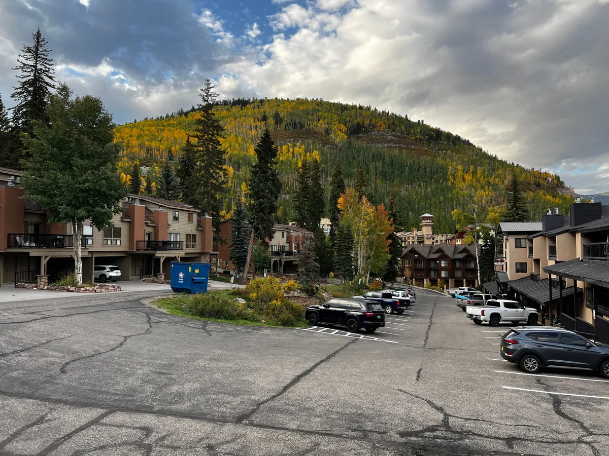 A picturesque exterior scene featuring colorful autumn trees, mountains, and the charming architecture of the Purgatory Townhomes community. Vehicles in the parking lot suggest group arrivals and easy access for friends gathering to explore the area.