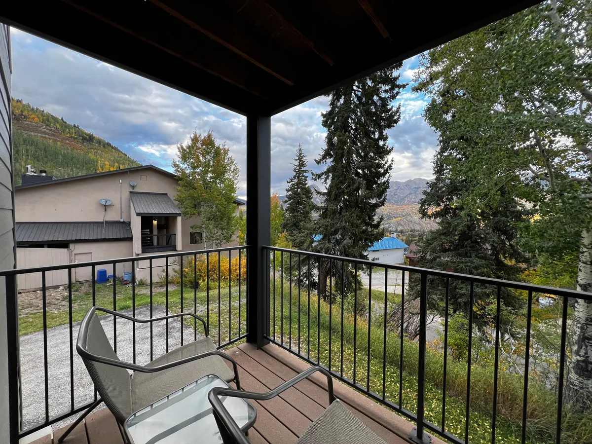A peaceful balcony furnished with seating, overlooking trees and mountains. The scene invites relaxation after a day of adventures, with the tranquil natural environment visible just beyond the railing.