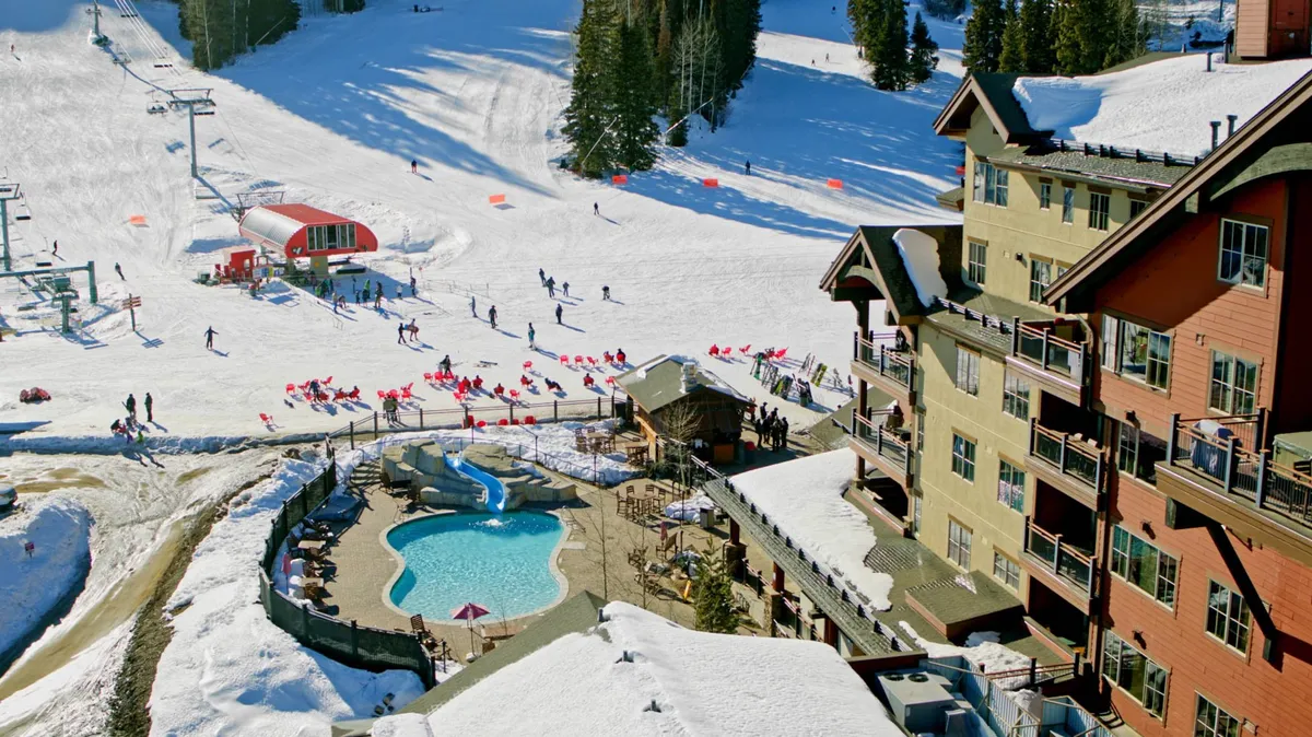 This exterior image features a heated swimming pool adjacent to ski slopes, with a ski lift, snow-covered landscape, and lodge architecture in the background. The scene is lively, showing both the pool and the resort's proximity to winter sports activities.