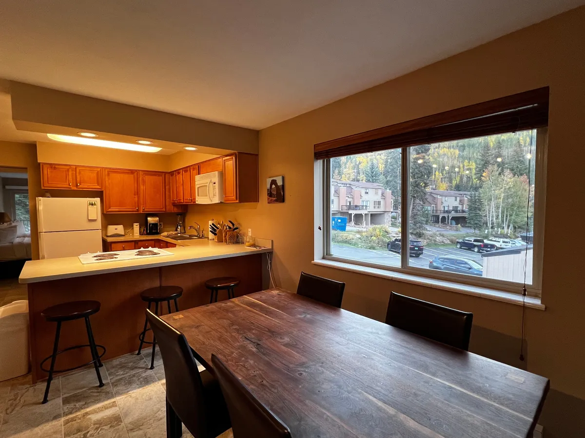 A dining area is showcased here, centered around a sturdy dining table set next to a window with beautiful views. The mood is warm and welcoming, perfect for family breakfasts, festive dinners, or sunlit conversations. The kitchen counter is nearby, emphasizing functionality and communal meals.