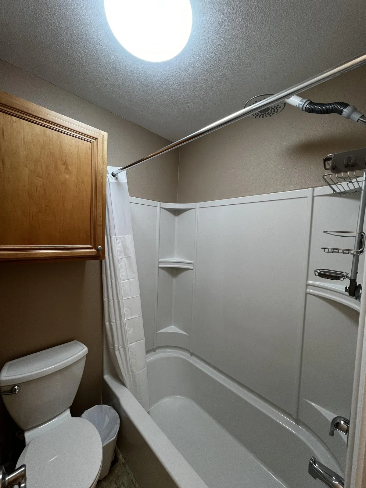 This bathroom features a toilet, bathtub with a shower curtain, wooden cabinet, and a neutral, practical layout. The space is functional and private—ideal for both quick routines and moments of solitude after a busy day.