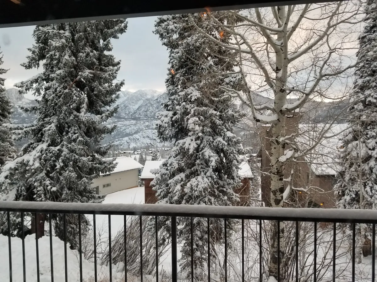 A beautiful winter view with snow-covered trees, mountain backdrop, and snowy rooftops. The tranquil scene hints at opportunities for outdoor adventures like skiing and snowboarding, as well as cozy indoor gatherings as the sun sets.